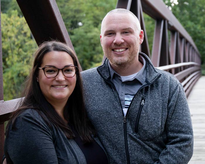 Melanie Hughes and her husband, Chad standing on a wooden bridge in a forest