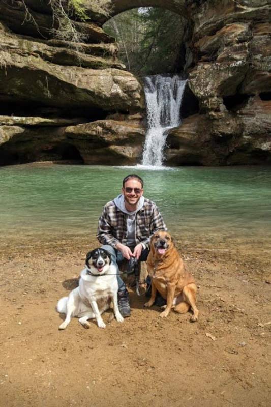 Dan Powell posing in front of a waterfall with his dogs